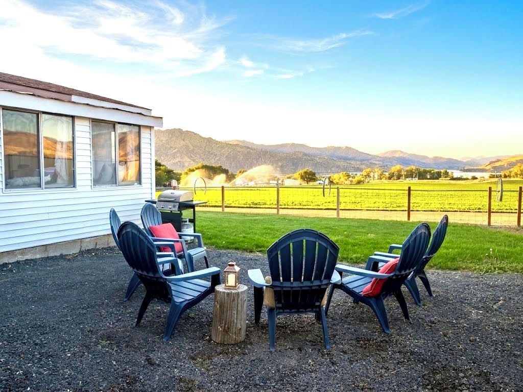 An outdoor seating area with chairs and a table, a wooden post, and a view of a field and mountains in the background.