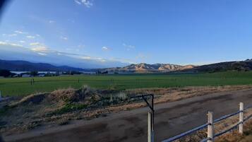 A rural landscape with a dirt road, green fields, and distant mountains under a clear sky.