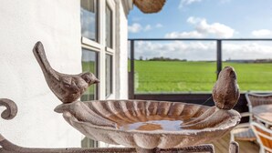 A rustic outdoor water feature with a bird-shaped spout and a decorative basin, set against a backdrop of a green field and a clear sky.