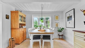 A dining area with a wooden table and chairs, a cabinet with glass doors, and a window with a view of greenery.