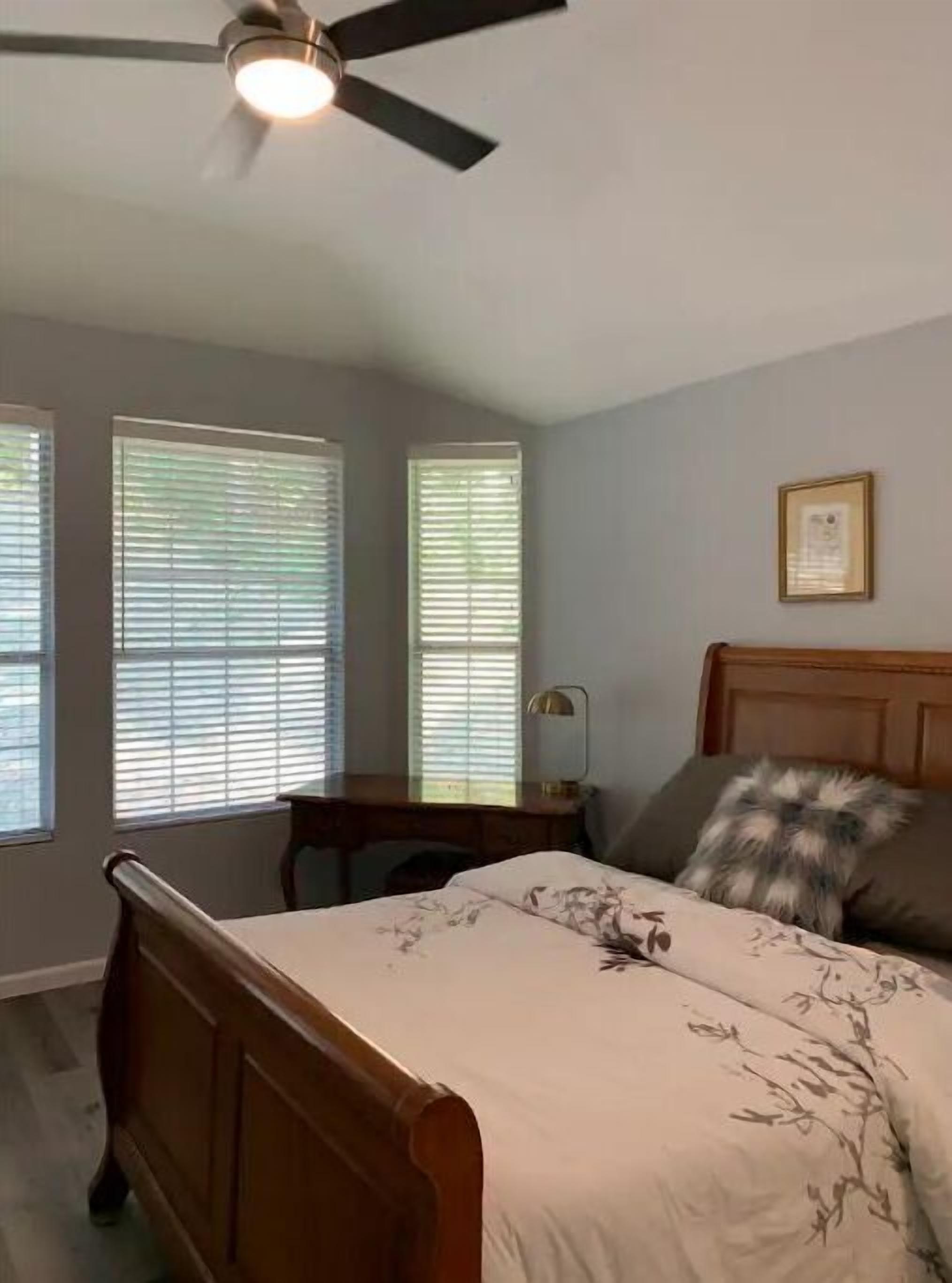 A bedroom with a bed, a desk, and a ceiling fan.