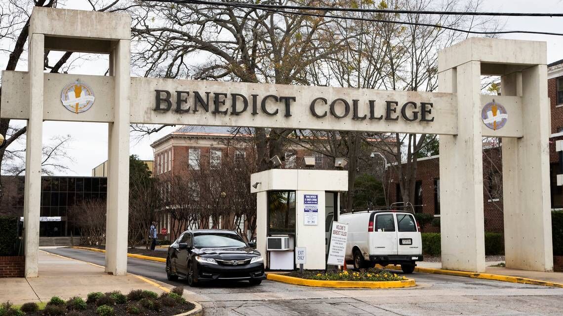 L’entrée du collège Benedict, avec un panneau indicateur, un espace de stationnement et un fourgon blanc.