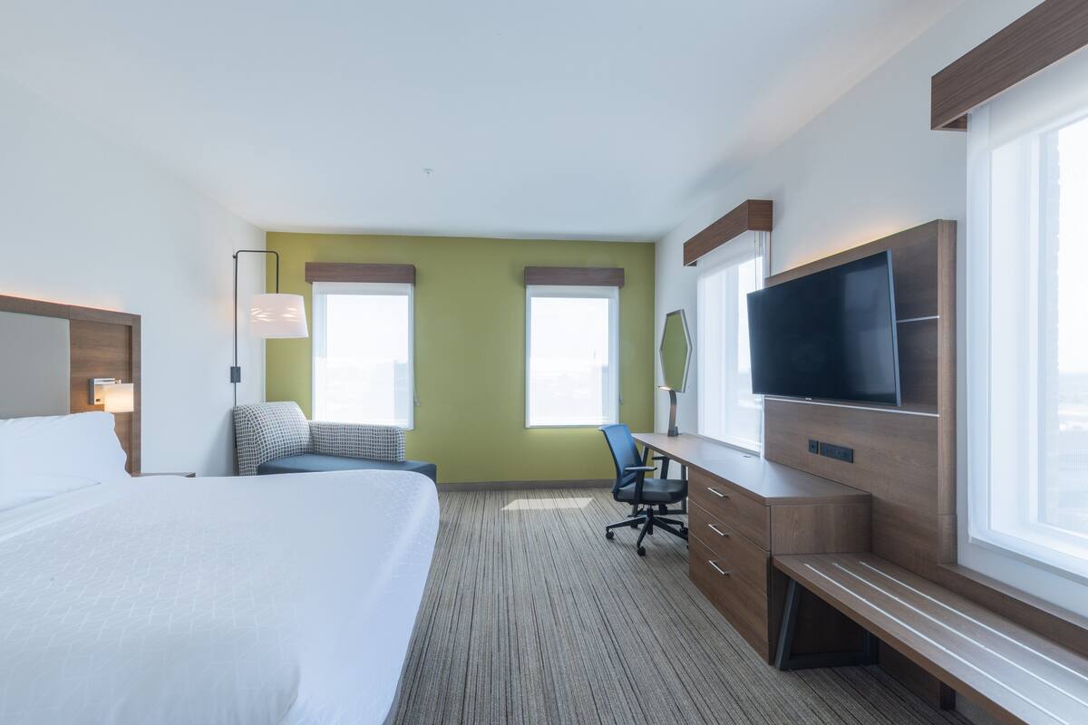 A hotel room with a large bed, a desk with a chair, a television, and two windows.