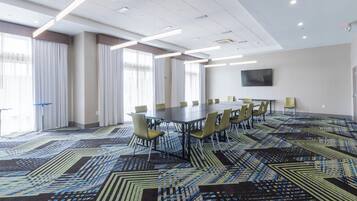 A conference room with a large table, chairs, a flat-screen TV on the wall, and patterned carpet.