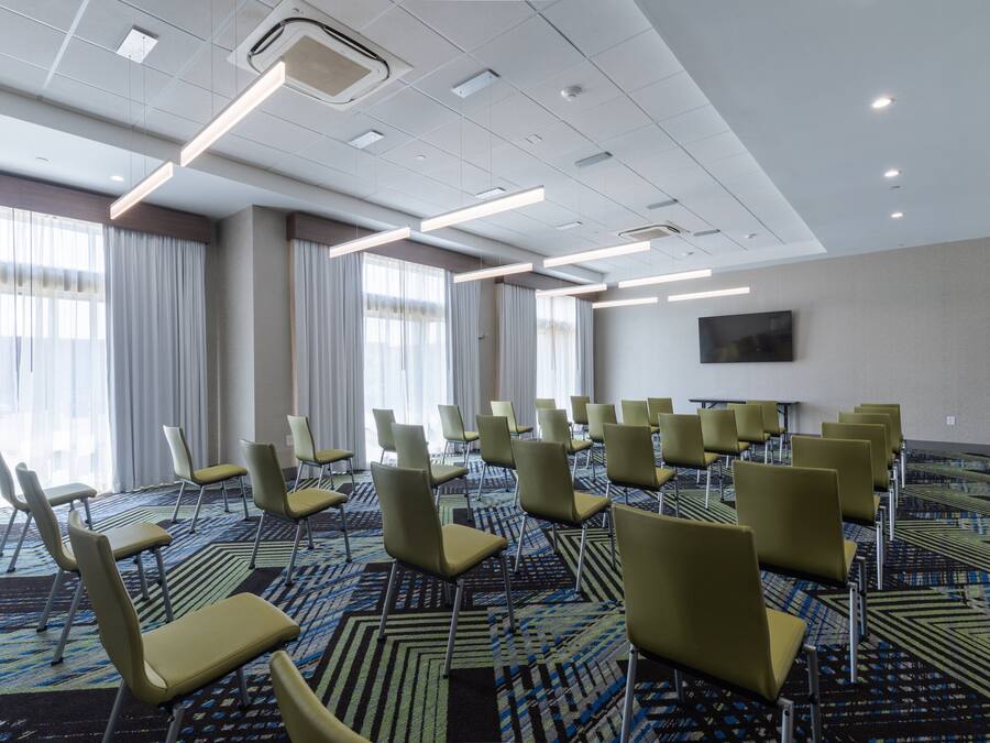 Un salón de conferencias con hileras de sillas, una alfombra estampada y un televisor de pantalla plana en la pared.