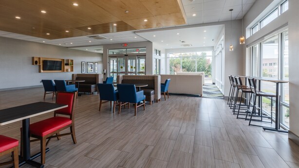 A spacious indoor area with wooden flooring, multiple seating arrangements including tables and chairs, and large windows providing natural light.