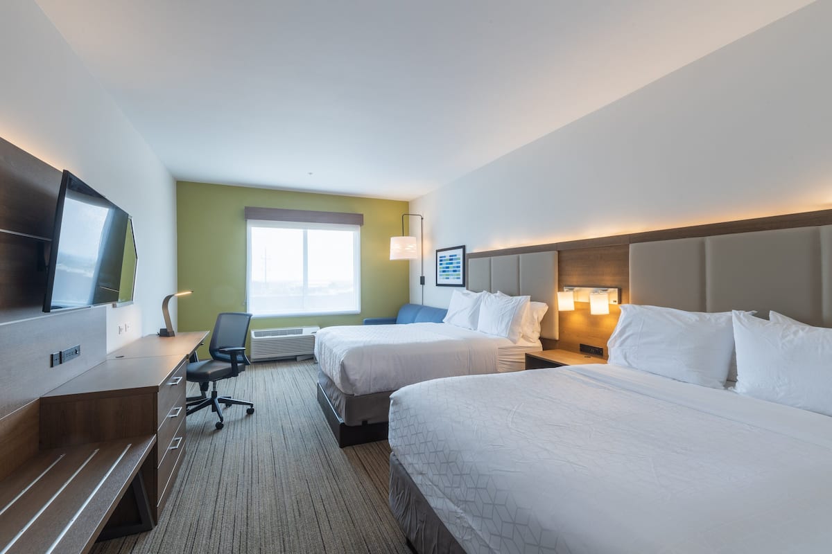 A hotel room with two beds, a desk, a chair, a TV, and a window.