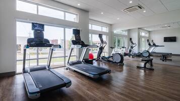 Une salle de sport équipée de tapis de course, de vélos d’appartement et d’un appareil d’aviron.