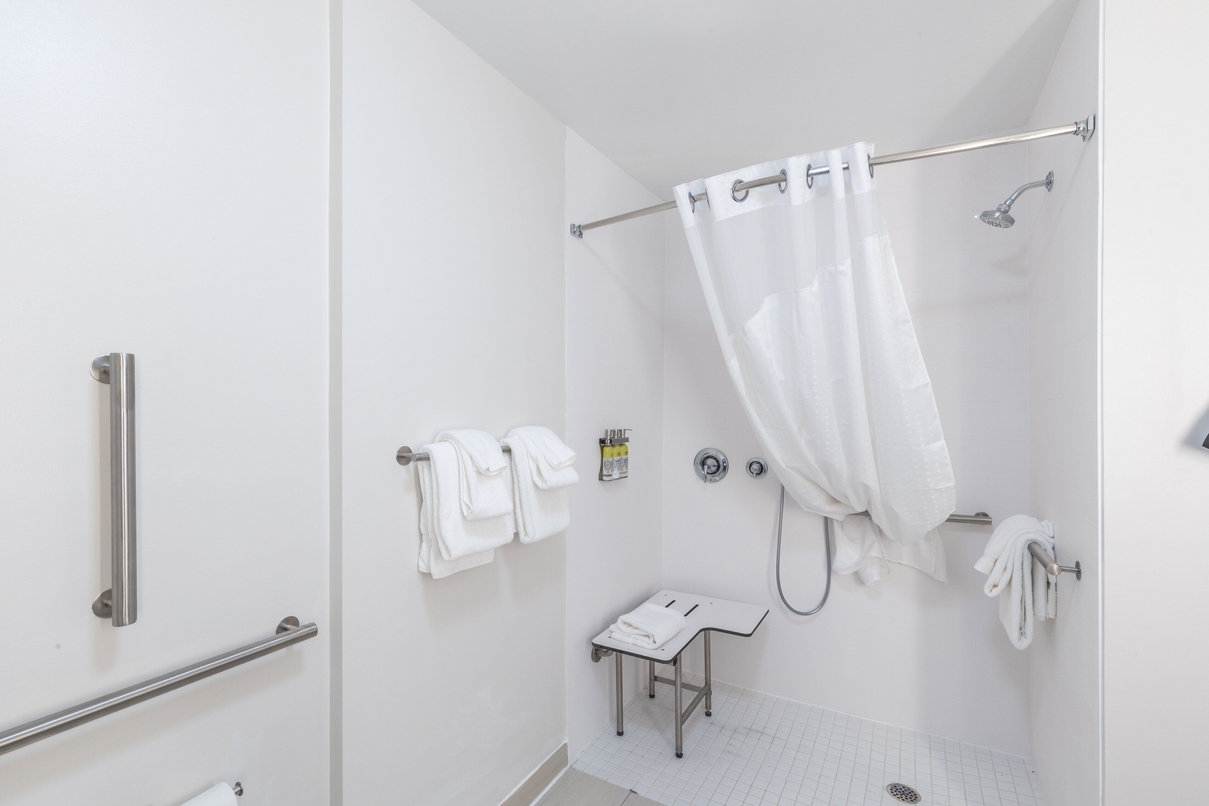 A modern bathroom with a shower, grab bars, a small table with a towel, and a toilet.