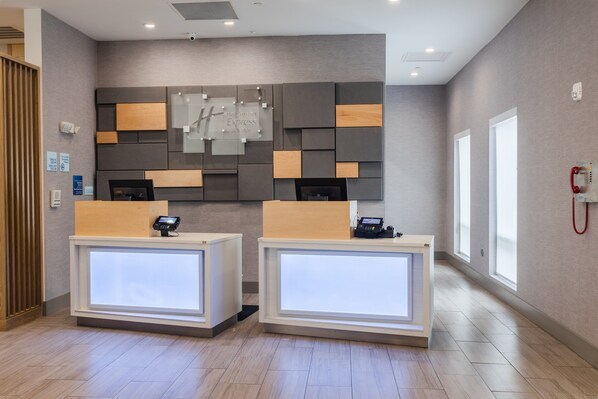 A hotel reception area with two reception desks, a modern wall design, and a visible phone on the wall.