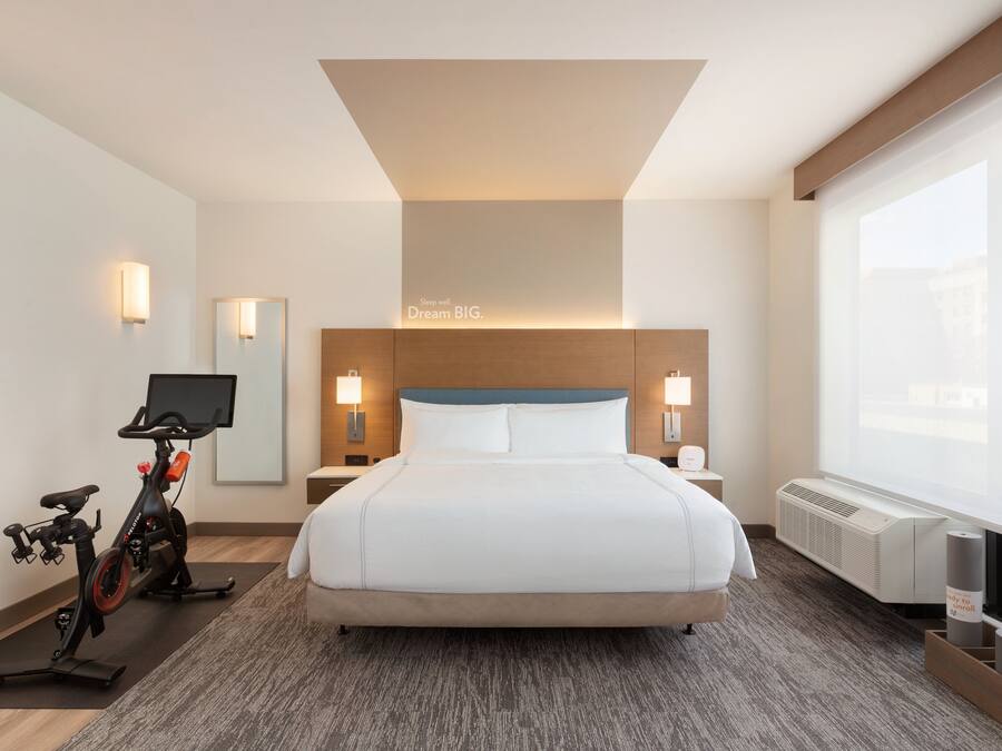 Una camera d'albergo con un letto grande, una televisione, una cyclette e vista sulla città dalla finestra.
