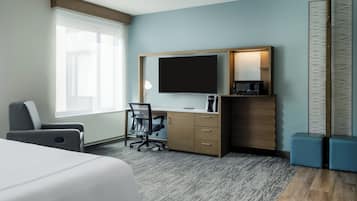 A hotel room with a bed, a desk with a TV, a chair, a coffee maker, and a large window.