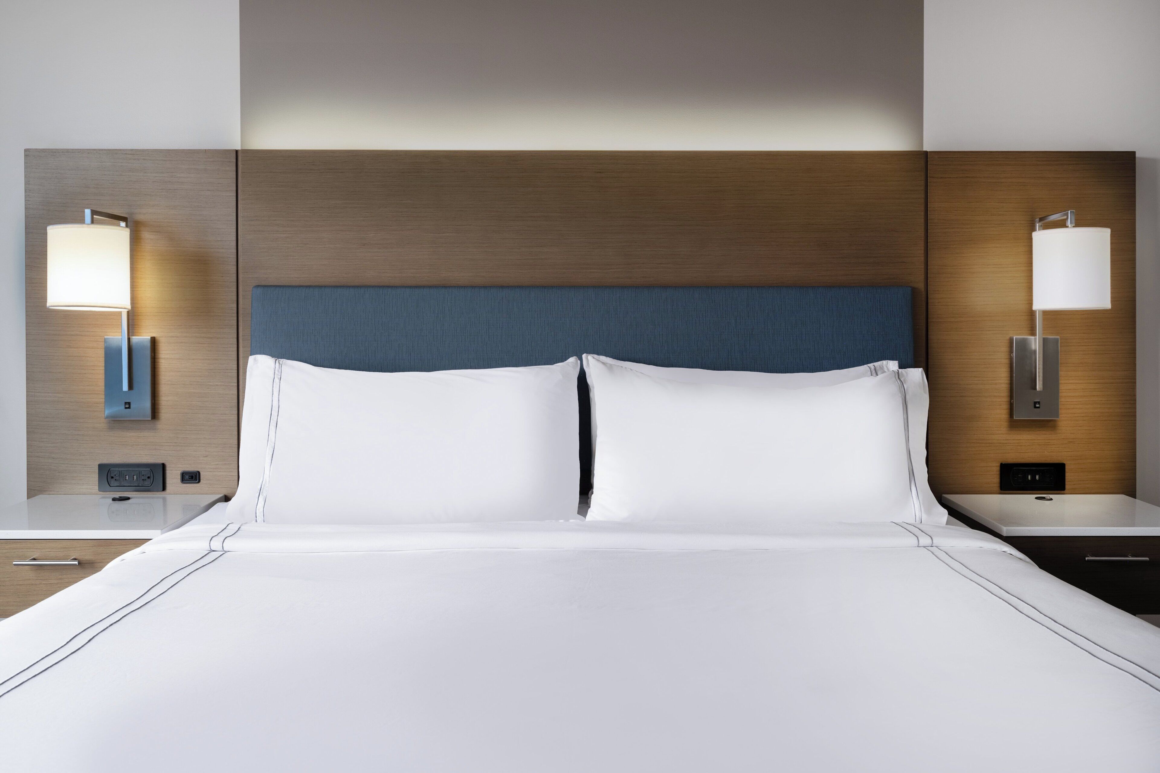 Hotelkamer met een groot bed, twee nachtkastjes, een wandlamp en een stopcontact.