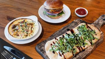 A table with a burger, a bowl of soup, and a pizza on a wooden board.