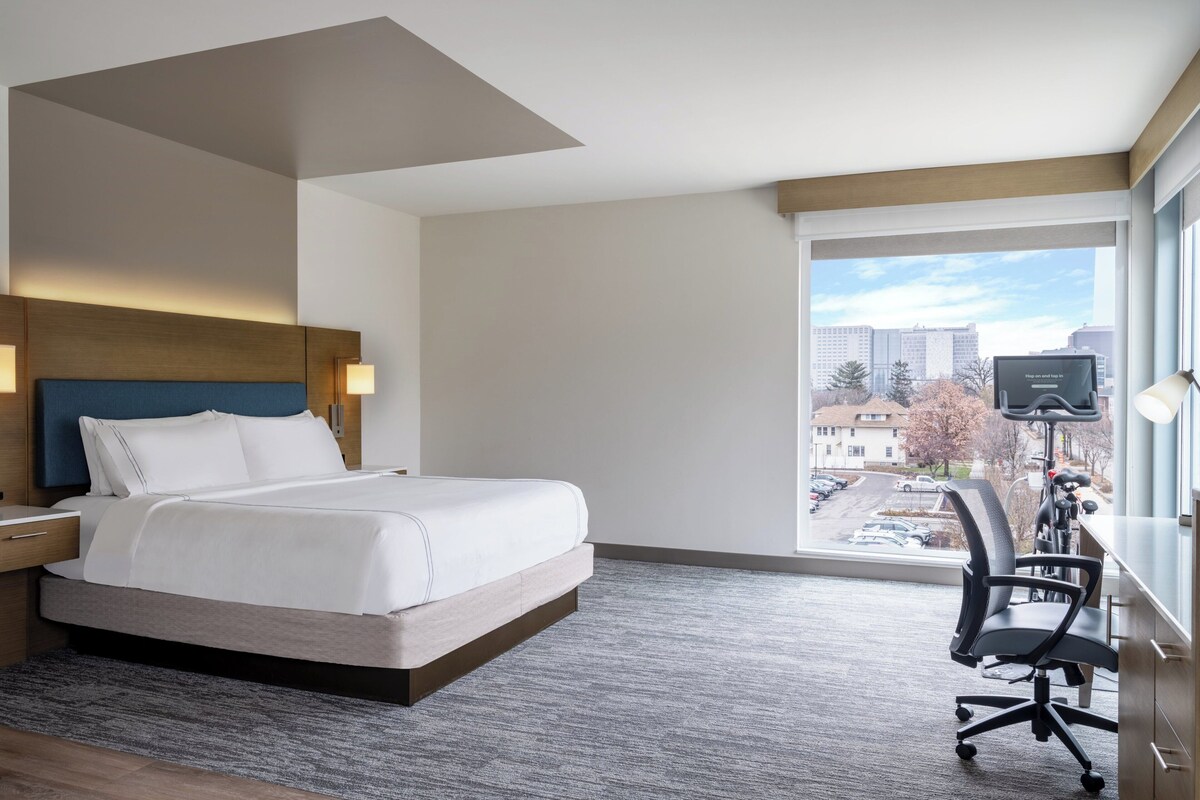 Een moderne hotelkamer met een groot bed, een bureau met stoel, een televisie en uitzicht op de stad.