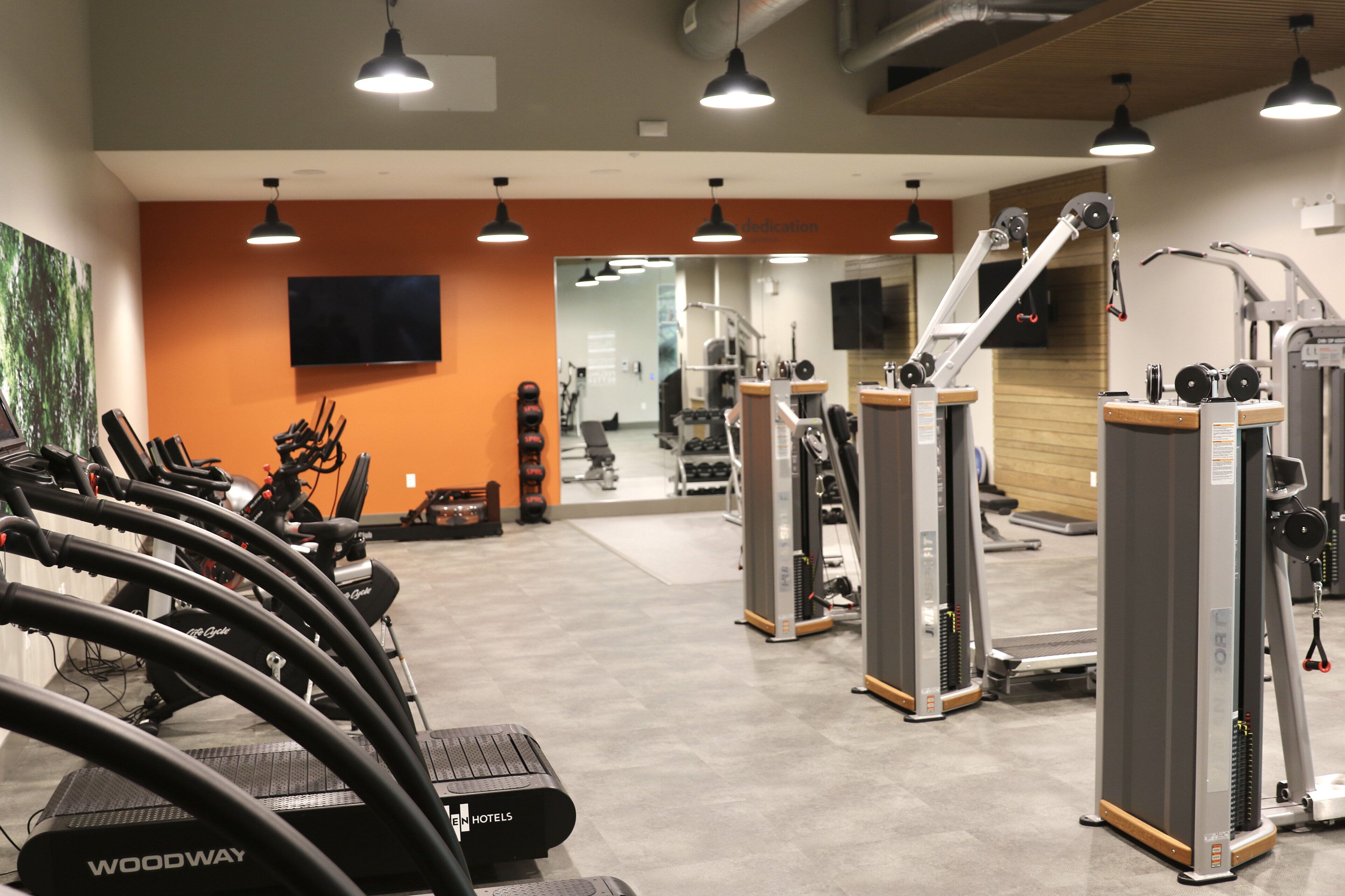 A gym with treadmills, weight machines, and a mirror wall.