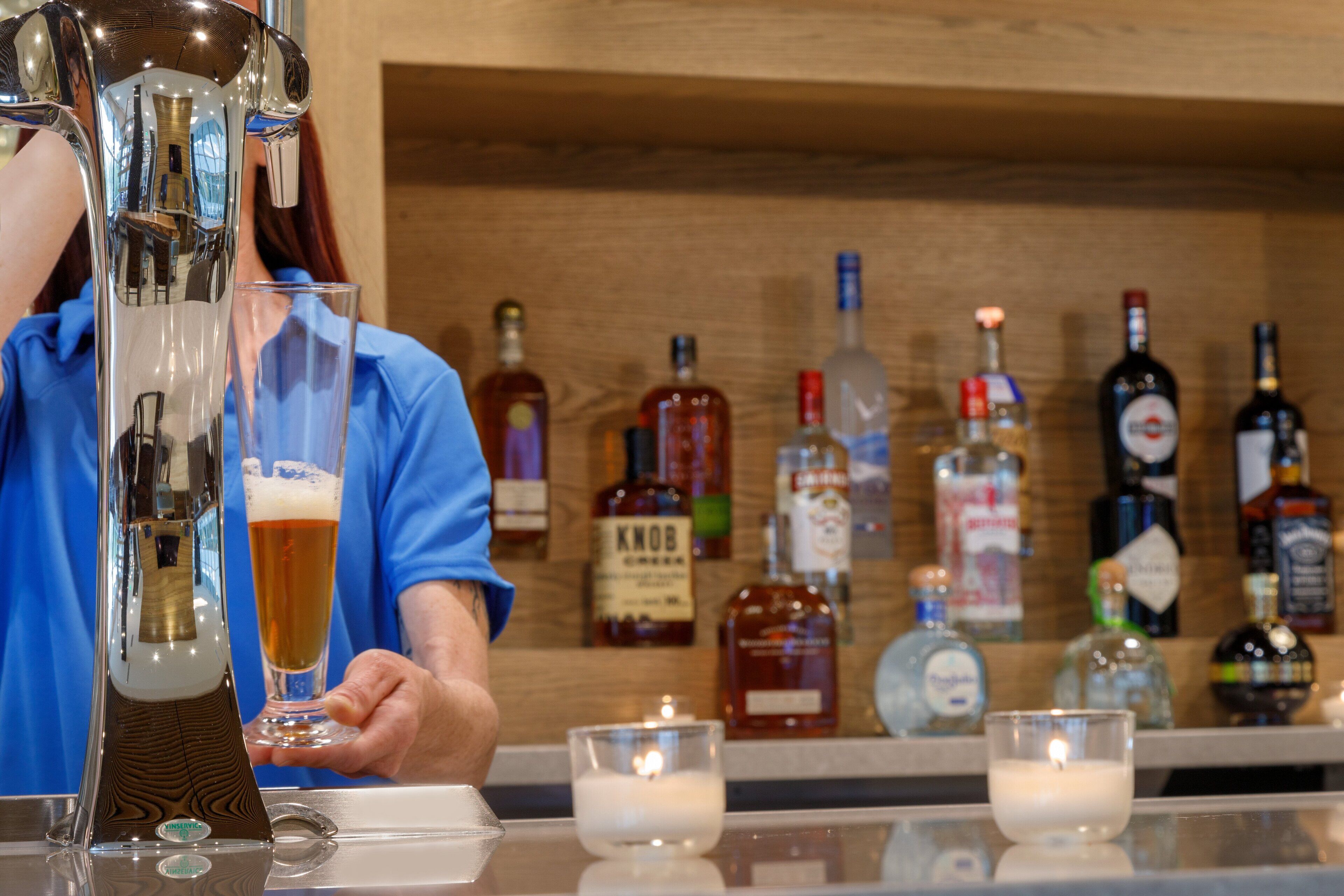 A bar area with a beer tap, a glass of beer, and various liquor bottles in the background.