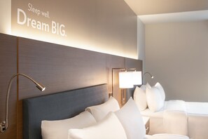 A modern hotel room with a large bed, a headboard, and a wall-mounted light fixture.