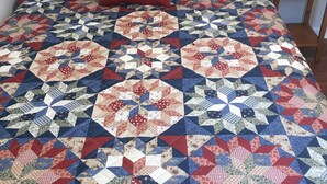 A bed with a quilt featuring geometric patterns and a red pillow.