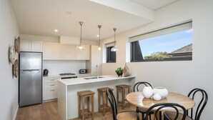 A modern kitchen with a central island, wooden stools, and a dining table with chairs. - Designer Penthouse Overlooking Manly, the Ocean and Harbour (Manly)