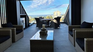 A modern outdoor seating area with wicker furniture and a glass-top table, overlooking a cityscape. - Designer Penthouse Overlooking Manly, the Ocean and Harbour (Manly)