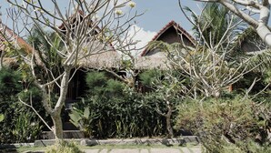 Um jardim tropical com uma casa de telhado de palha, vegetação exuberante e um caminho de pedra.