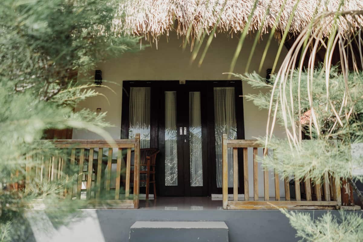 A wooden deck with a bench, a door with glass panels, and a thatched roof structure.