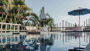 A clear pool with a wooden deck and palm trees, surrounded by a fence. - Sentulan Garden Villa (Penida Island)