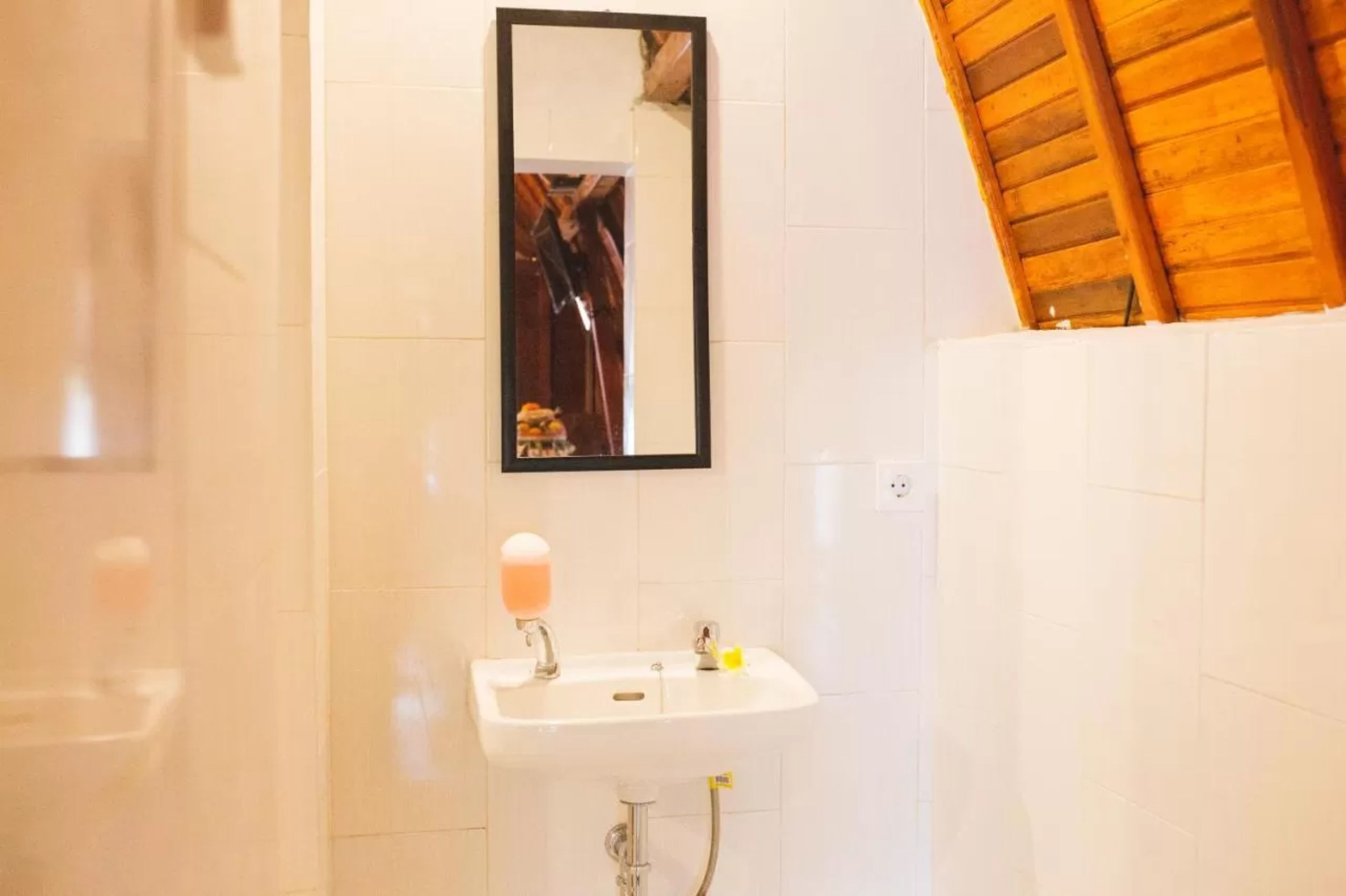 Casa de banho com lavatório branco, espelho e teto de madeira.
