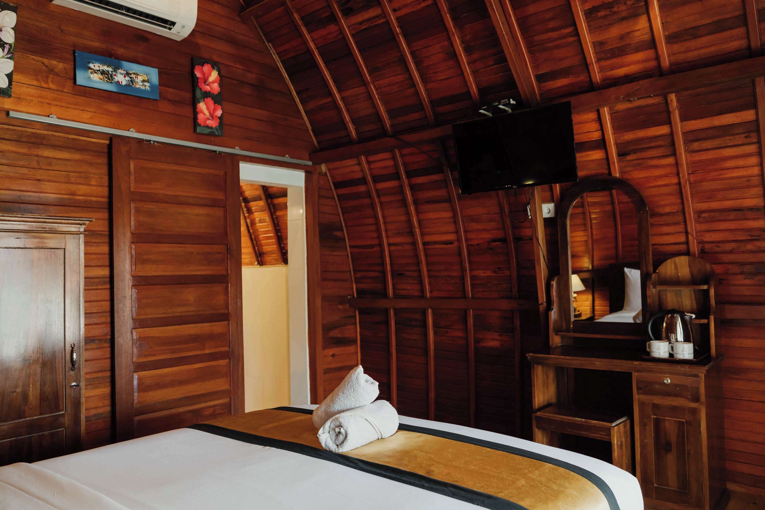 Een kamer met houten lambrisering, een bed, een televisie en een houten bureau met een spiegel.