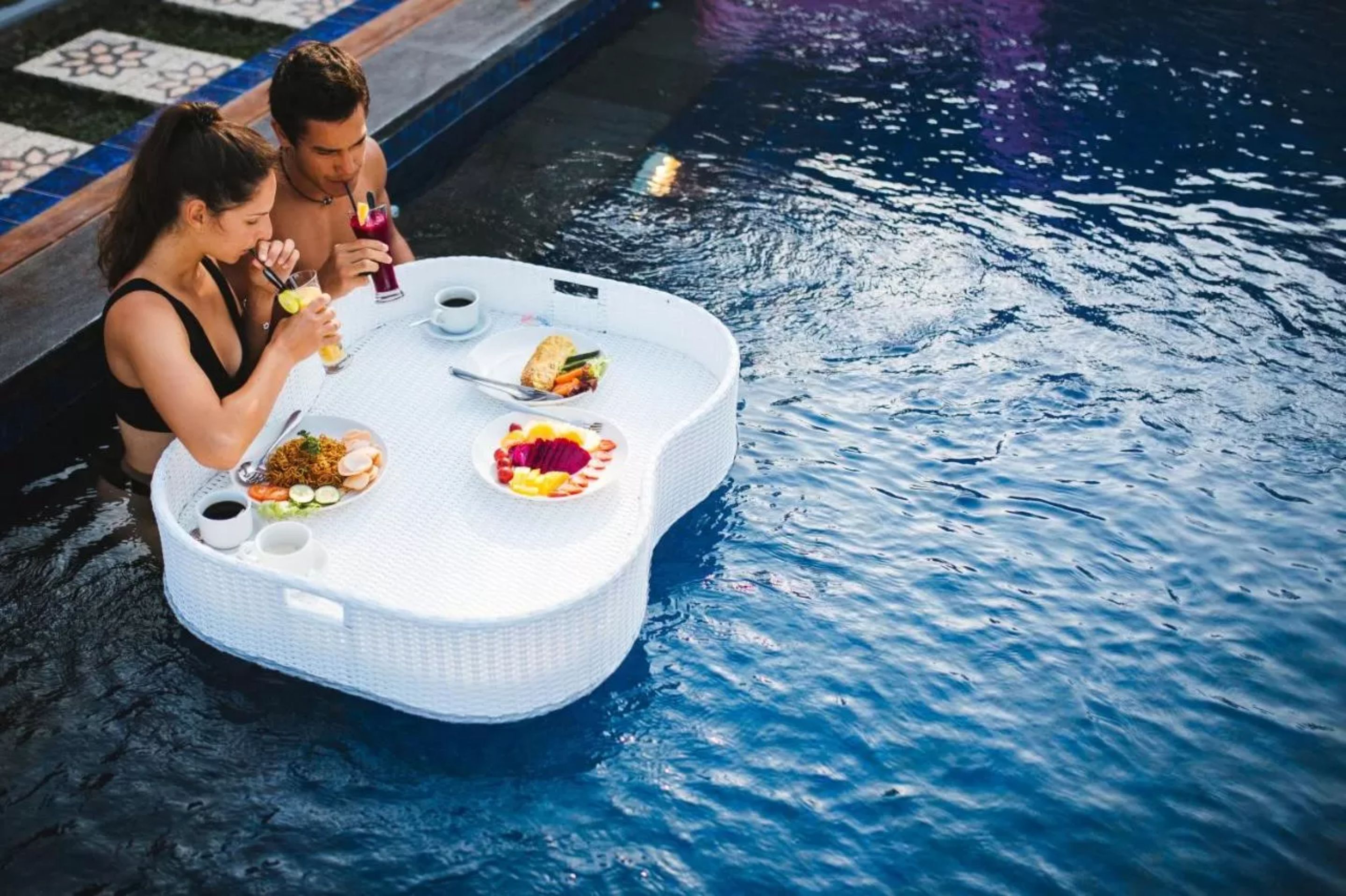 A couple dining at a floating table by a pool.