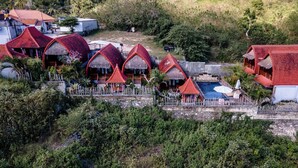 A resort with multiple thatched-roof cottages, a swimming pool, and a stone wall surrounding the property. - Sentulan Garden Villa (Penida Island)