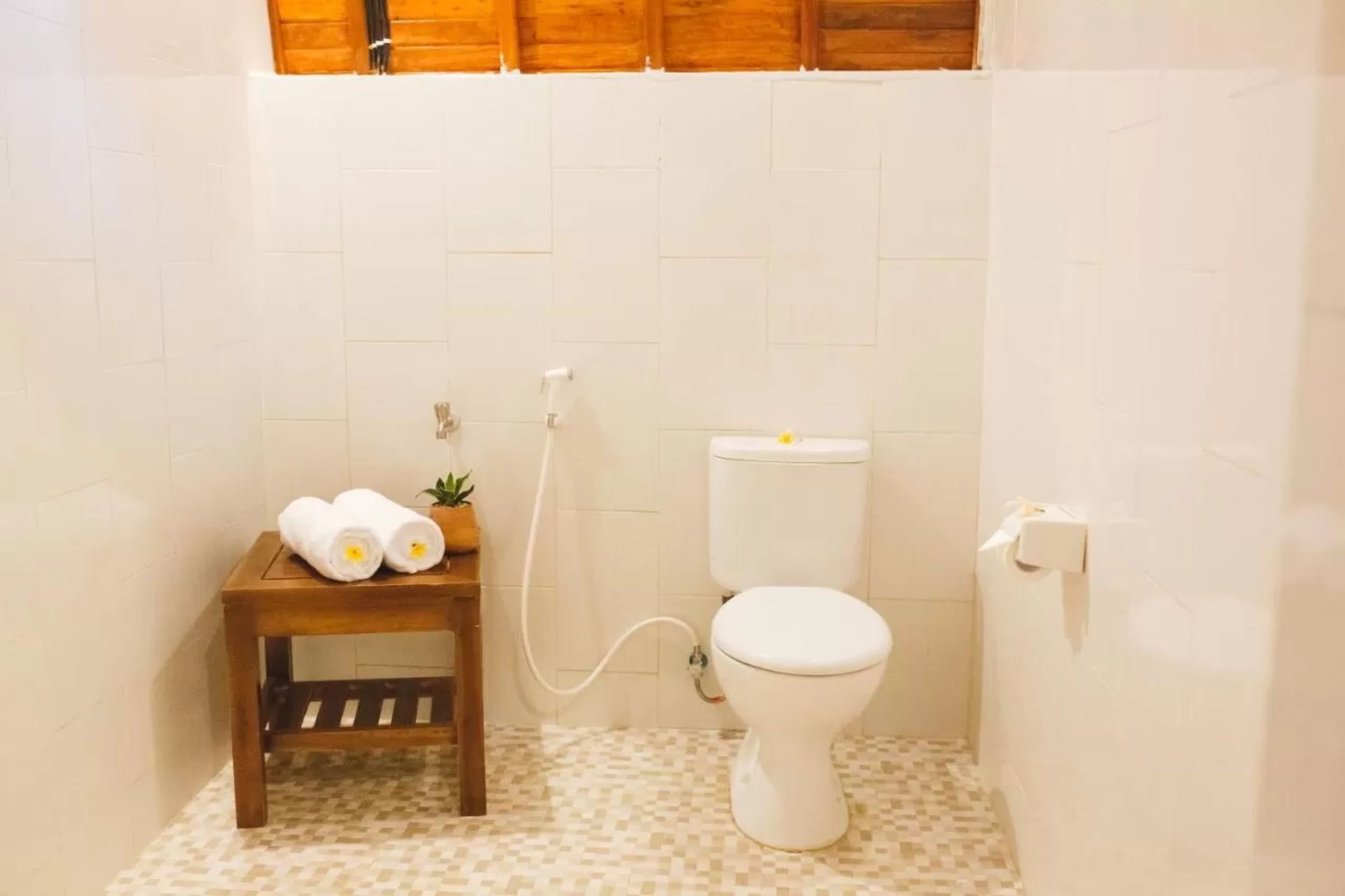A small bathroom with a toilet, a wooden stool with towels, and a small plant.