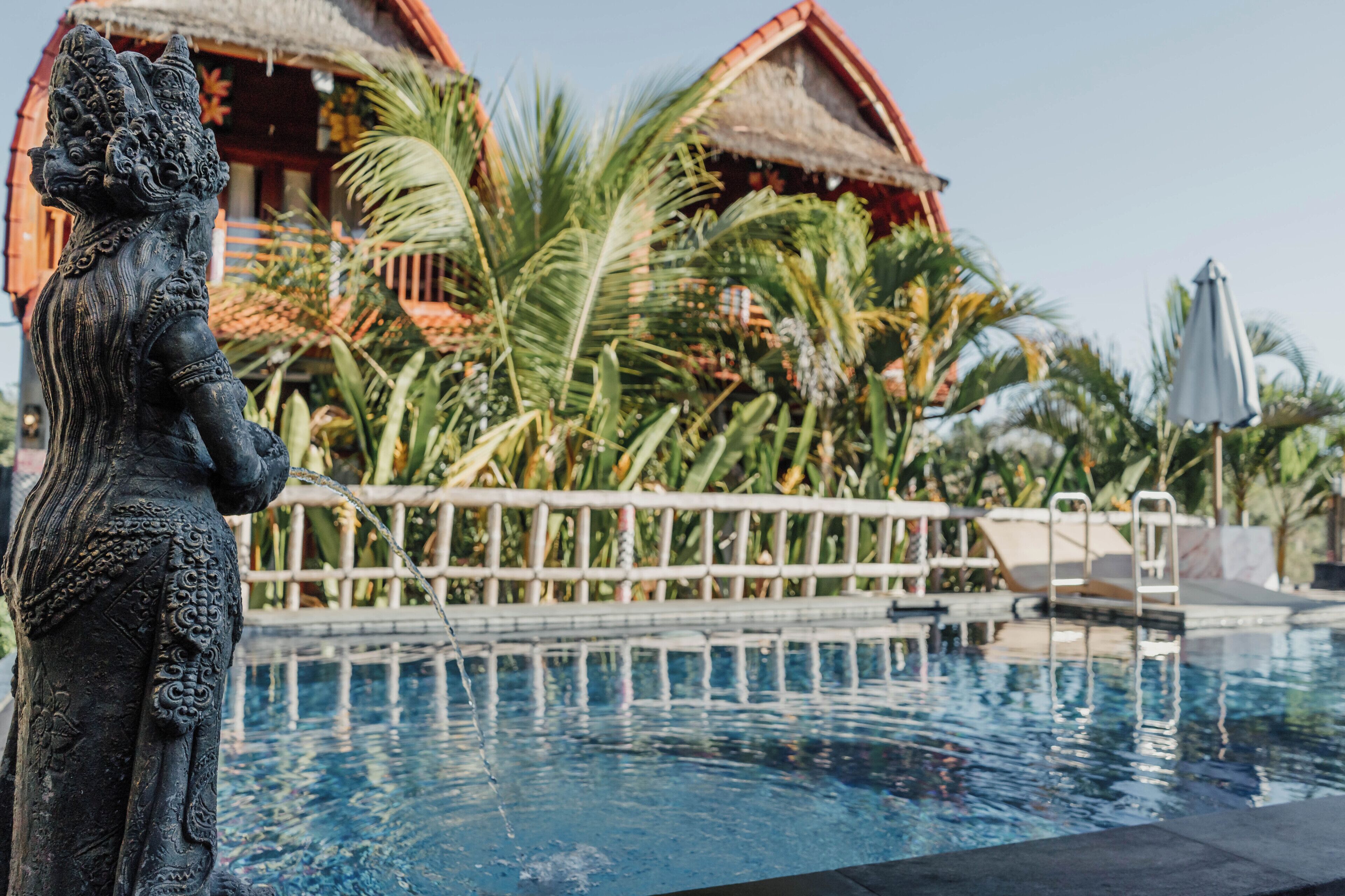 A statue by a pool with thatched-roof buildings in the background.