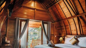 A wooden cabin room with a bed, curtains, a nightstand, and a view of the outdoors. - Sentulan Garden Villa (Penida Island)