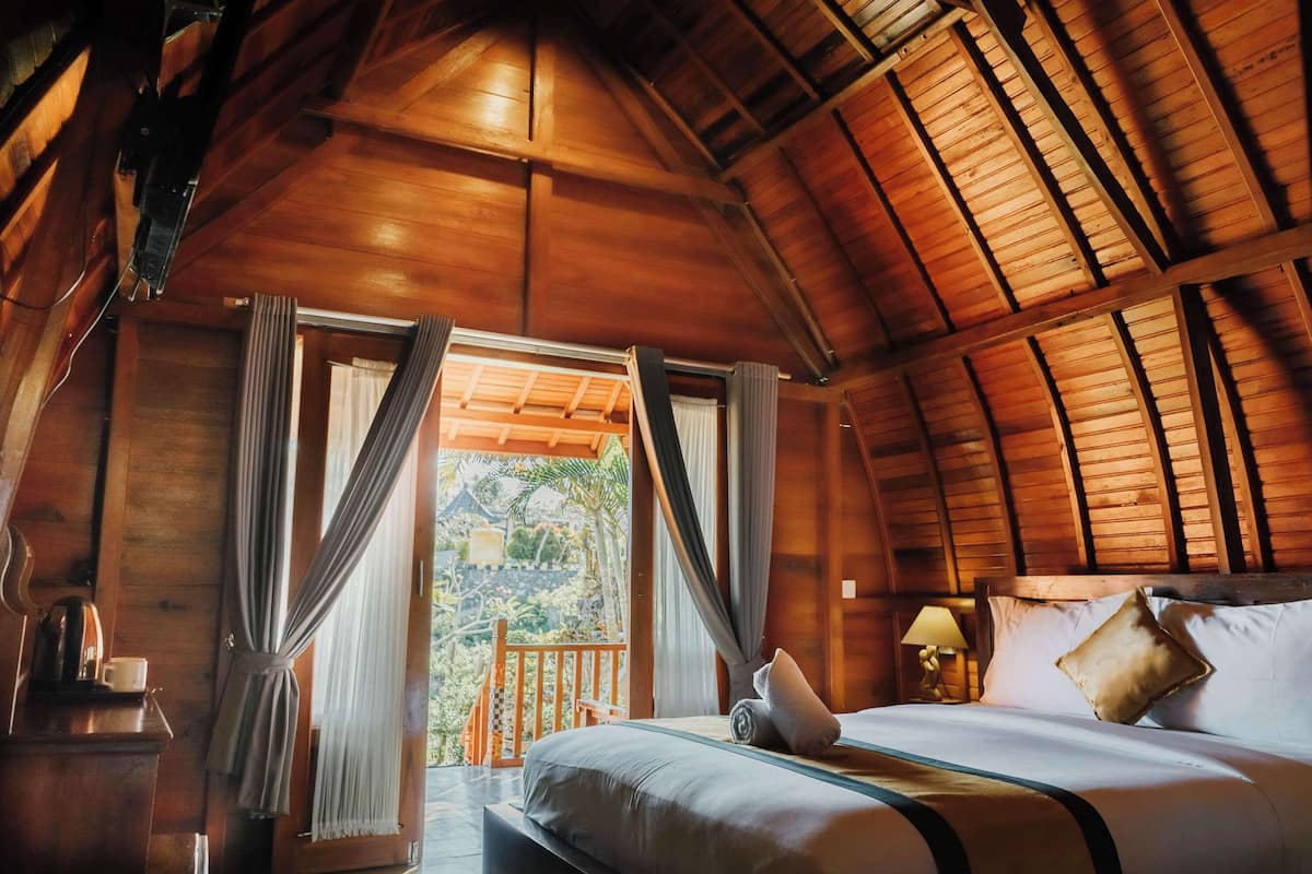 Une chambre rustique en bois, avec un lit, des rideaux, une table de chevet et une vue sur l’extérieur.