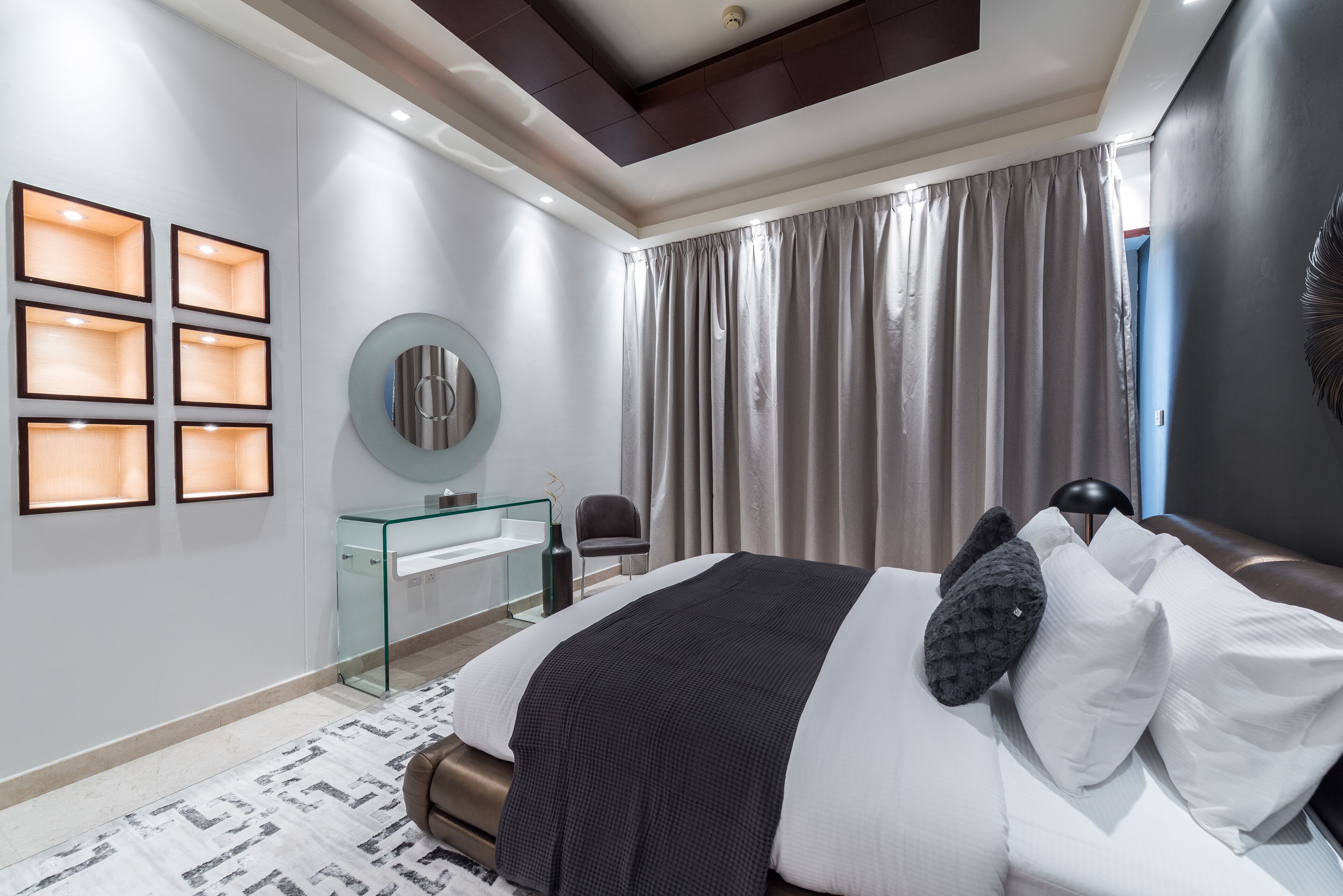Un dormitorio moderno con una cama grande, un escritorio de cristal y un espejo en la pared.