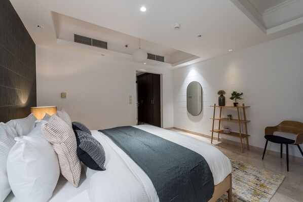 Une chambre moderne avec un grand lit, une table de chevet, un miroir et une étagère en bois ornée de plantes.