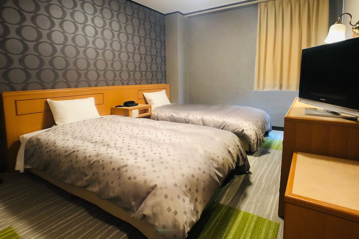 Ein Hotelzimmer mit zwei Betten, einem Fernseher, einem Schreibtisch und einer Lampe.