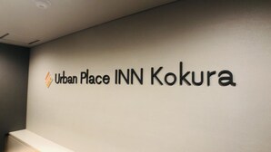 Un mur sur lequel est inscrit le texte « Urban Place INN Kokura », indiquant le nom de l’hôtel.