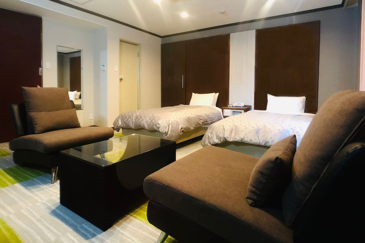 Ein Hotelzimmer mit zwei Betten, einer Couch, einem Couchtisch und einem Kleiderschrank.