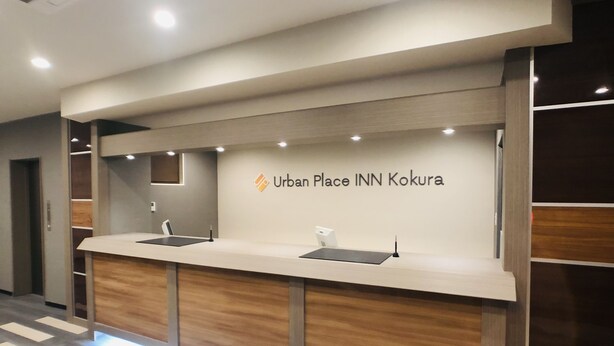 Un comptoir d’accueil avec une enseigne indiquant « Urban Place INN Kokura ».