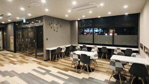 Un espace repas moderne, avec une horloge au mur, un sol à motifs et une vue sur l’extérieur grâce à de grandes fenêtres.