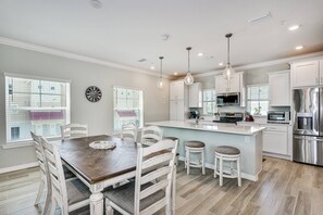 Une cuisine moderne avec des meubles blancs, un îlot central, des appareils en acier inoxydable et des luminaires suspendus.