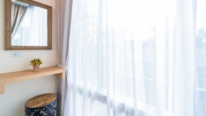 A room with a wooden shelf, a small plant, a round wooden stool, and sheer curtains. - Charcoal Panwa Beach (Wichit)
