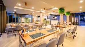A modern dining area with multiple tables and chairs, a sofa, and a kitchen area in the background. - Charcoal Panwa Beach (Wichit)