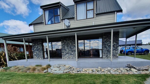 A modern two-story house with a stone foundation, large windows, and a covered patio area. - Private holiday home (Twizel)
