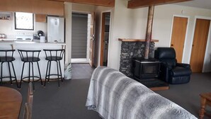 A living room with a stone fireplace, a bar area with stools, and a sofa. - Private holiday home (Twizel)
