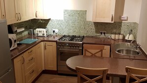Una cocina compacta con armarios de madera, una estufa a gas, un lavamanos y una mesa redonda con dos sillas.