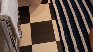 Un baño con suelo a cuadros, inodoro, lavamanos y un perchero para toallas.